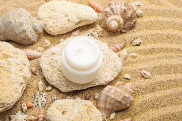 A jar of moisturizing face cream, sun protection cream on the sand with stones and shells. Summer concept.Beauty and spa concept