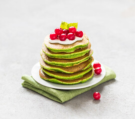 Vegan spinach pancakes with green matcha tea with berries on a plate on a light gray background