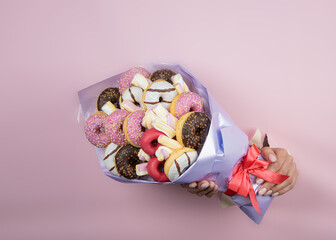 Edible bouquet of donuts and muffins in hand on a pink background. There is a place for text...