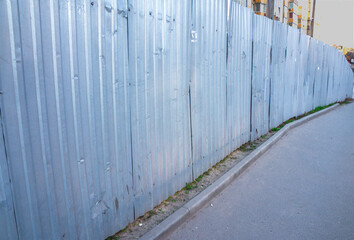 A metal fence along the sidewalk. Fences of the construction site. enclosure, fencing, guard