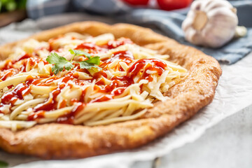 Deep-fried tastyful hungarian cheesy langos with poured ketchup, herbs and garlic