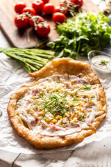 Tasty hungarian langos served with sour creme, ham, cheese, herbs and vegetables in the background