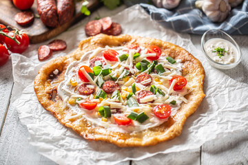 Traditional hungarian combo made of deep fried crusty langos with garlic edges, precisely served with cream, grated cheese, tomatoes and domestic sausages also with extra cream in little bowl