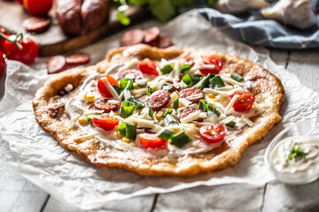 Traditional hungarian combo made of deep fried crusty langos with garlic edges, precisely served with cream, grated cheese, tomatoes and domestic sausages also with extra cream in little bowl