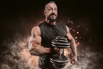 Muscular man posing with a dumbbell on a background of fire and smoke. Fitness and bodybuilding...