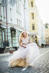 Pretty smiling young woman with long blond hair in elegant flying light dress running along the street