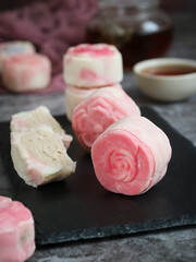 A non baked traditional colorful fragrant Asian snow skin mooncake in a rose shape with taro filling with cut piece, tea in background.  Usually eat chilled and served to celebrate Mid-Autumn Festival