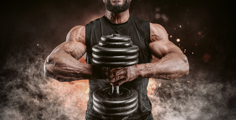 Muscular man posing with a dumbbell on a background of fire and smoke. Fitness and bodybuilding...