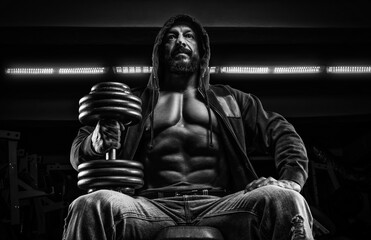 Muscular man sits on a bench with a dumbbell in the gym. Fitness and bodybuilding concept.