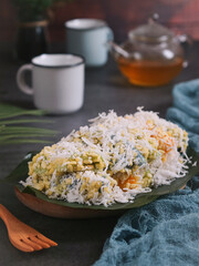 A plate of natural colorful Thai tradition dessert soft mung-bean rice stuffed with grated fresh coconut or Kanom Tua Pap in thai, cup and pot of tea in background. It had a chewy and soft texture 
