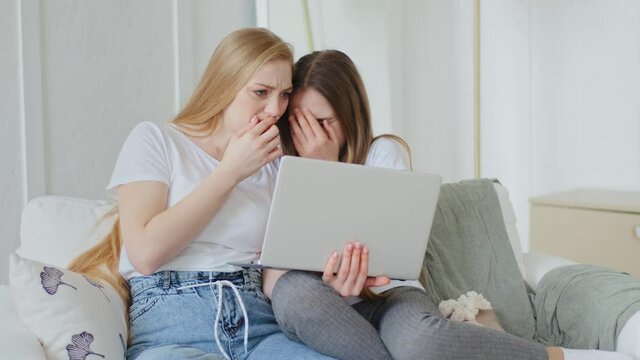 Caucasian caring adult mother and daughter teenager girl child watching horror movie at home using modern laptop cover mouth with hands from surprise shock schoolgirl hides eyes from fear of disgust