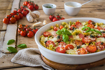 Pasta casserole with basil pesto sauce, tomatoes and mozzarella, vegetarian, on an old wooden table