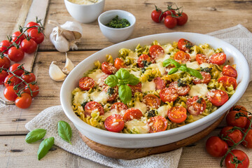 Pasta casserole with basil pesto sauce, tomatoes and mozzarella, vegetarian, on an old wooden table