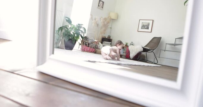 Mirror image of baby girl crawling in living room