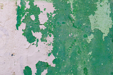 The old wall painted with green paint is destroyed and the paint is peeling off
