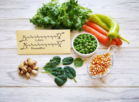 Foods rich in lutein and zeaxanthin with structural chemical formulas of two carotenoids. Fresh vegetable as best food sources of lutein and zeaxanthin. Spinach, carrot, peas, corn, pepper, lettuce.