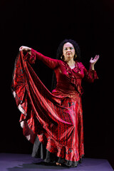 Gypsy woman with curly black hair in a red dress flutters her skirt on a black background.