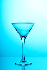 Studio photo of empty transparent martini glass on light blue background. Silhouette of triangular shape glass for coctails