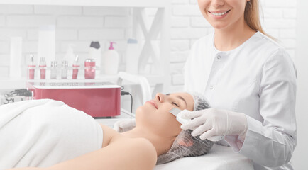 Side view of smiling young beautician in white rubber gloves doing procedure with equipment for young beautiful woman. Concept of different procedure anti-aging in professional beauty salon.