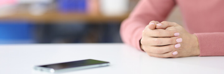 Womens hands lying on table near mobile phone closeup