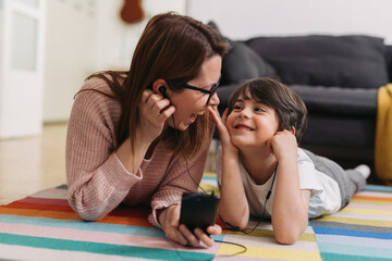 mother and child listening music on headphones using smartphone.