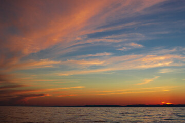 Long dramatic majestic clouds on blue sky with yellow pink tones in sunset blazing, scenic seascape of calm sea in dusk