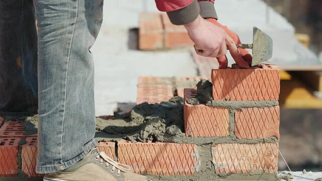 Close up of a man building a brick house. Laying red bricks on a construction site on a sunny day. House construction close up.