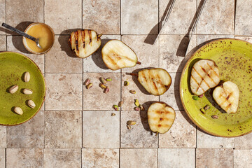 Tasty grilled green pears with pistachio nuts served with honey on green craft plate and earth toned tales from above