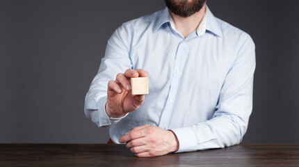 A businessman in a shirt holds one wooden cube in his hand. Empty. Office. Workplace. Office worker.