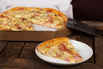 Slice of pizza in white plate with a pizza box in the background; pizza of pork loin with cream cheese and pineapple or lombo ao creme com abacaxi