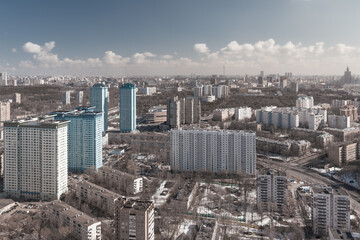 Aerial view of residential areas of a large city with multi-storey buildings against a blue sky with light clouds in early spring with snow on the ground and trees without foliage