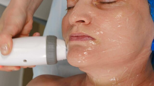 Facial lifting, wrinkle smoothing and rhytide effacement procedure. Hardware cosmetology treatment. Beautician moves manipulator with light on female face. Non-surgical face skin lifting in beauty