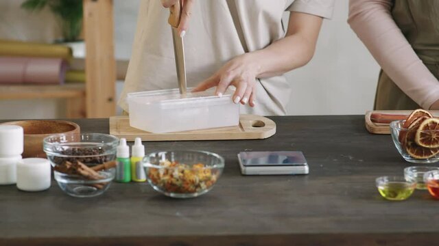 Midsection PAN shot of woman cutting premade soap base with knife using melt and pour method of making natural diy soap customizing it with spices, dried fruits and flowers