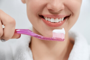 Close up young beautiful woman cleaning teeth with pink toothbrush in bathroom. Concept of care for...