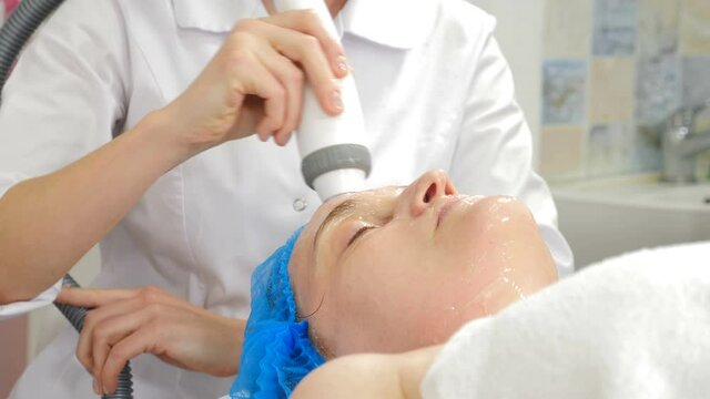 Facial lifting, wrinkle smoothing and rhytide effacement procedure. Hardware cosmetology treatment. Beautician moves manipulator with light on female face. Non-surgical face skin lifting in beauty