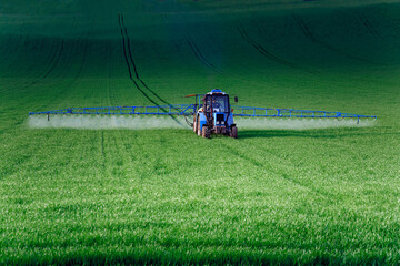 A tractor with attachments performs agricultural work in a green field. Business in industrial...