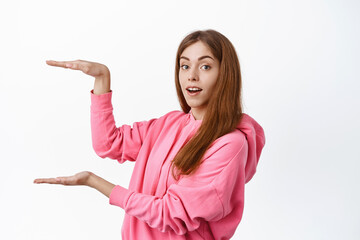 Young caucasian woman display product, holding big object, showing product on white copy space, recommend something, white background