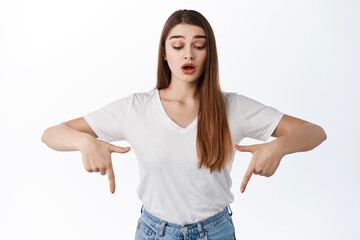 Surprised attractive woman open mouth, say wow and look down, pointing bellow on bottom, showing...