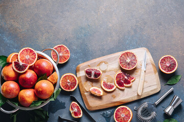Summer cocktails and fresh orange juice cooking concept. Whole and sliced blood oranges with shaker and bartender utensils over blue table background. Flat lay, top view, copy space.