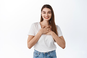 Smiling thankful girl appreciate nice gesture, holding hands on heart grateful, say thank you, standing heartfelt and touched against white background