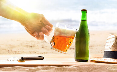 Hand with beer mug celebrating holidays with beach background.