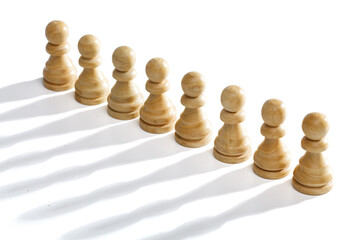 A row of white pawns on a white background with a long shadow. White wooden chess pawns, close-up.