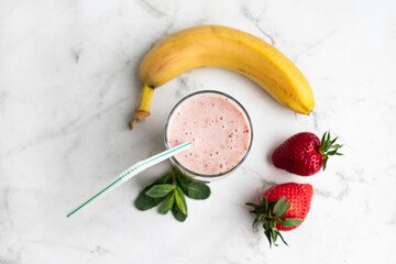 Smoothie with strawberries and banana in a transparent glass, banana, strawberries and mint on a light background, top view. The concept of proper nutrition.