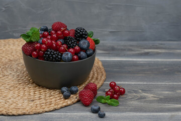 Ripe sweet different berries in bowl on wooden table. Harvest Concept.