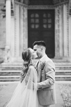 Groom hugs and kisses bride against the background of the entrance to the Basilica of Santa Maria Maggiore, Rome, Italy. Black and white photo
