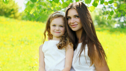 Portrait of beautiful happy smiling mother with little girl child on the grass in a summer park