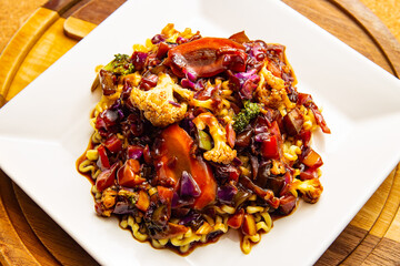 Um prato branco quadrado com yakisoba vegetariano.