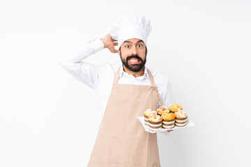 Young man holding muffin cake over isolated white background frustrated and takes hands on head