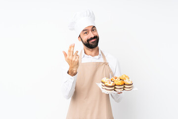 Young man holding muffin cake over isolated white background inviting to come with hand. Happy that you came