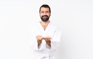 Young man doing karate over isolated white background holding copyspace imaginary on the palm to...